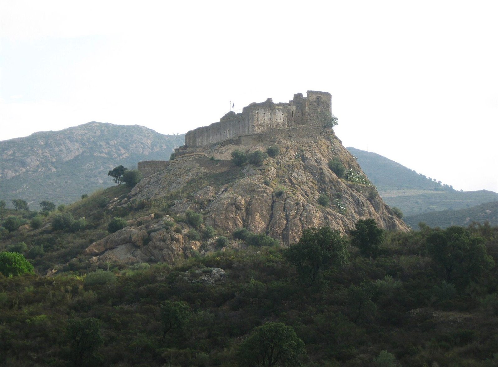 Castell de Quermançó dalt d'un turó rocós envoltat de vegetació, a Vilajuïga
